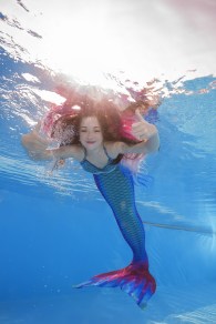 A girl in a mermaid costume poses underwater in a pool